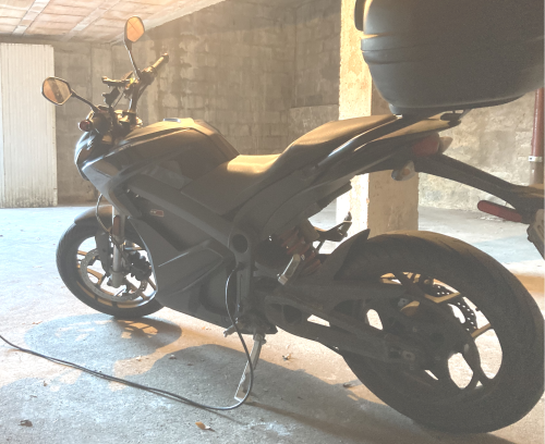 Une moto électrique garée dans un garage  branchée avec un câble secteur