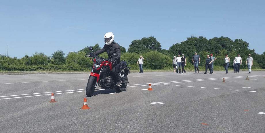 Moto en premier plan faisant un slalom, derrière els piéon